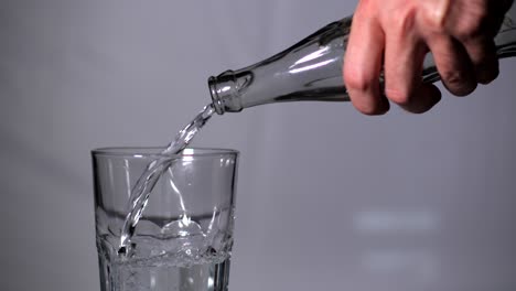 Man's-Hand-Pouring-Water-Into-a-Drinking-Transparent-Glass-From-Bottle-on-Studio-Background---closeup