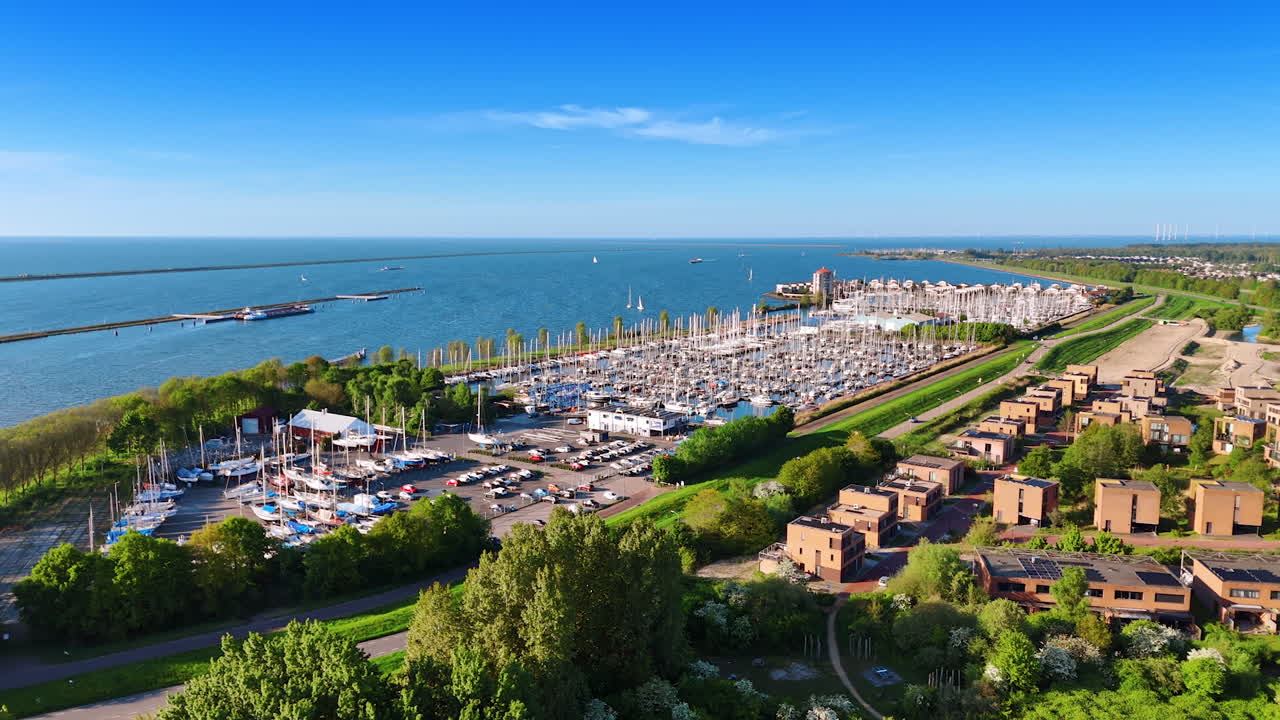 Yacht club with numerous boats and parking lot nearby. Drone flight above the green cityscape. Spectacular view of marina at backdrop. Lelystad, the Netherlands.