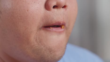 close up of a fat asian man's mouth eating fast food having fried chicken on a sofa in the living room at home