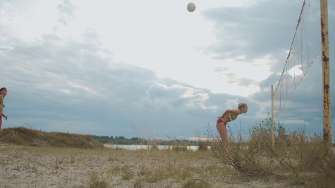 en el partido de competición por voleibol de playa los equipos femeninos compiten jugando en la cancha de arena pasando la pelota y atacando