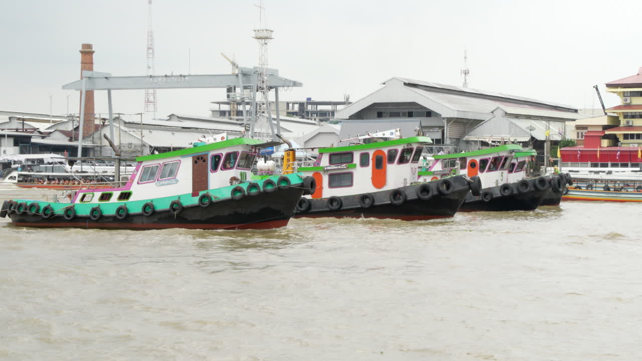 Slow motion of three tug boats moving along the Chao Phraya River, a major waterway in Bangkok, Thailand.