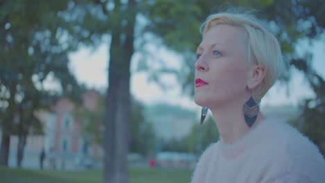 Profile-of-blonde-middle-aged-woman-sitting-in-park-and-smoking-cigarette,-close-up-slow-motion