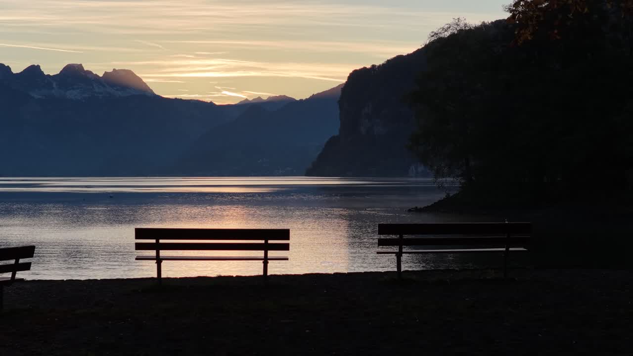 Tramonto sereno sul lago di Walenstadt in Svizzera, con tenui riflessi delle montagne e del cielo dorato sull'acqua calma