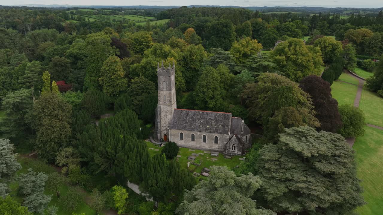 Chiesa di San Salvatore, Glaslough, Contea di Monaghan, Irlanda, Settembre 2022. Drone che si muove lentamente a sinistra orbitando attorno alla chiesa circondata da alberi fitti con la torre che spunta sopra la chioma.