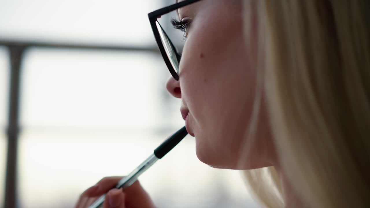 vista cercana de la cara de la dama con gafas y pluma en los labios reflejando algo, perdida en el pensamiento con un fondo suave y borroso, mostrando un momento reflexivo y reflexivo