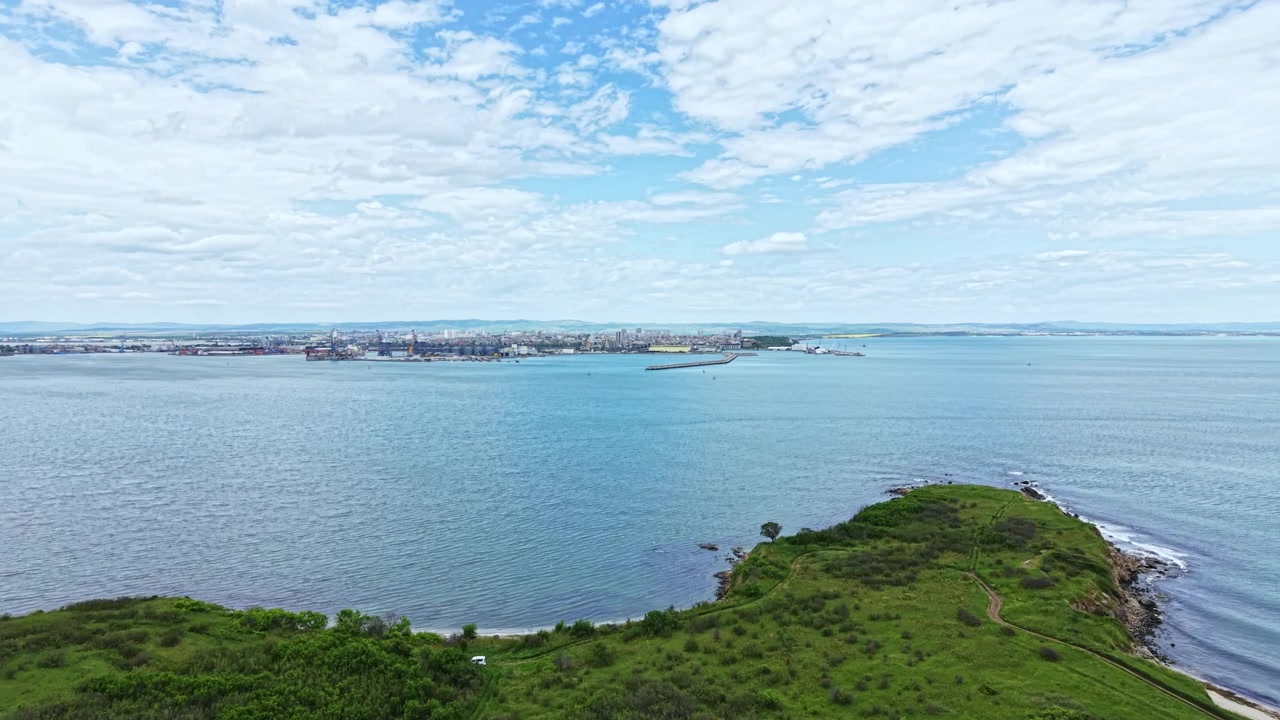 海岸近くの晴れた日、緑の丘と水辺、そして背景に都市のスカイラインが広がる眺め。