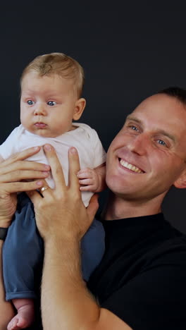 happy male wearing black t-shirt holding his infant son on the shoulder. little baby looking around and father kisses him on the cheek. vertical video