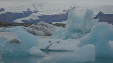 Glaciers-floating-in-Glacier-Lagoon,-Iceland,-with-seagulls-flying-overhead,-against-the-backdrop-of-blue-waters-moving-towards-Diamond-Beach