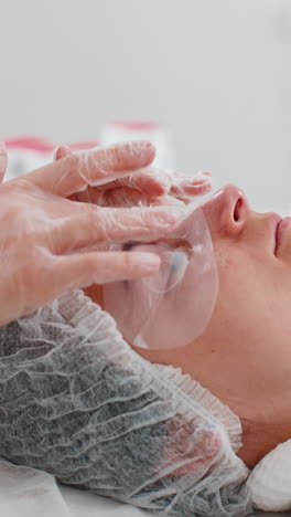 esteticista aplicando una máscara hidratante de regeneración en la piel y los ojos de la cara de una mujer adulta joven