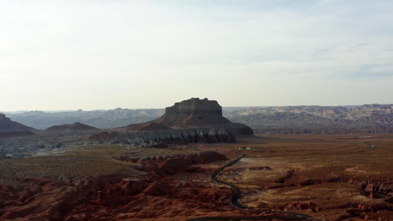 una muñeca en la escena del desierto de drones aéreos con un camino estrecho y sinuoso rodeado de rocas rojas y arena con grandes formaciones rocosas de butte rojo y blanco en el fondo en el parque estatal goblin valley utah