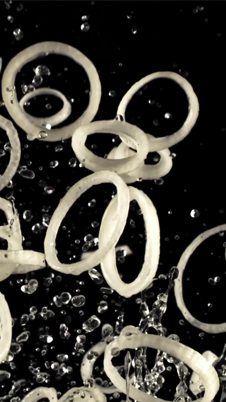 Cincin Bawang Jatuh ke dalam Air dengan Percikan di Latar Belakang Hitam
