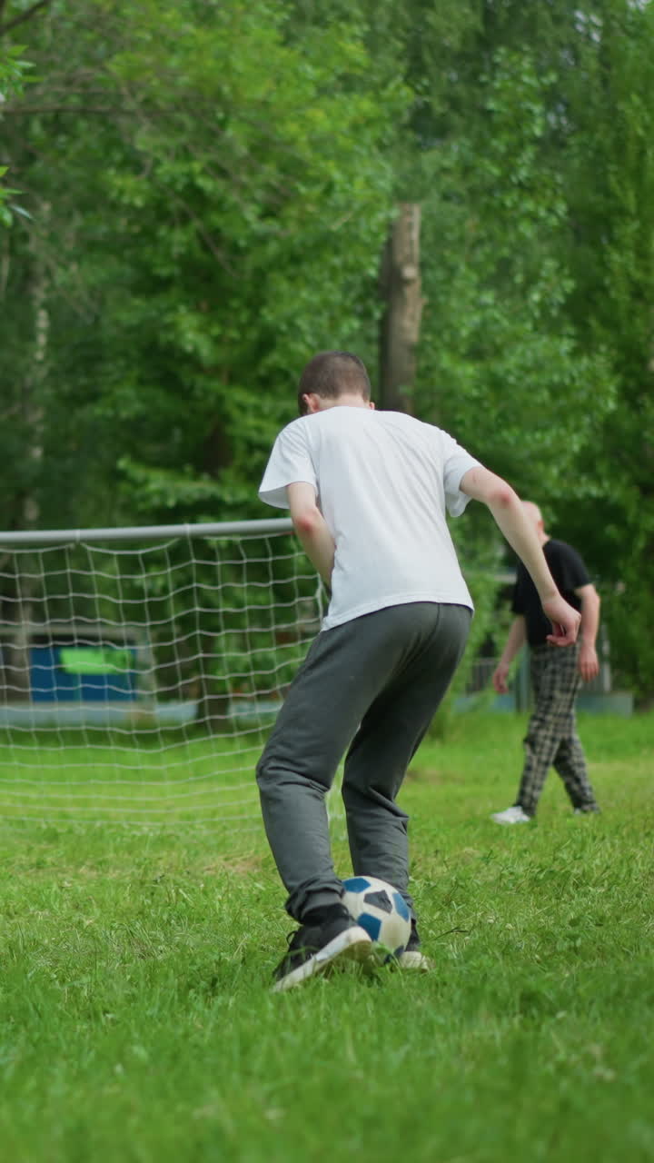 A young boy skillfully lifts a soccer ball with his leg, demonstrating his athleticism, in the background, his grandfather and younger brother can be seen