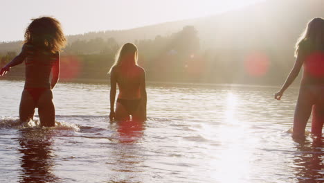 three female friends on vacation wading into lake at sunset