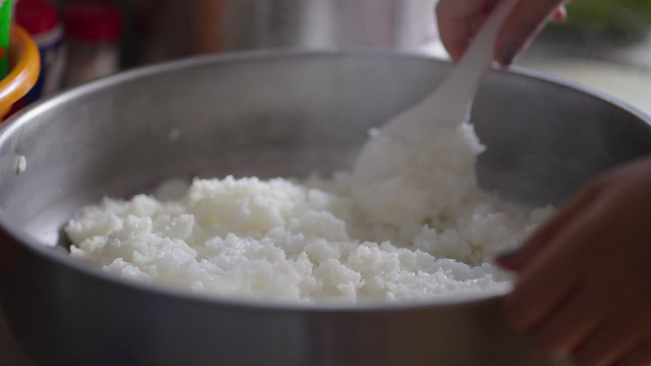 Close up of woman's hands stirring steaming rice in pot