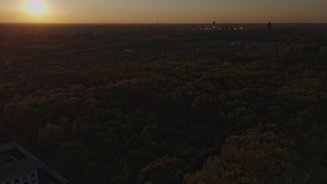 Aerial sunset shot over Leipzig, Germany. The skyline features the Völkerschlachtdenkmal (Monument to the Battle of the Nations), a vast forest area. Warm golden light during twilight.
