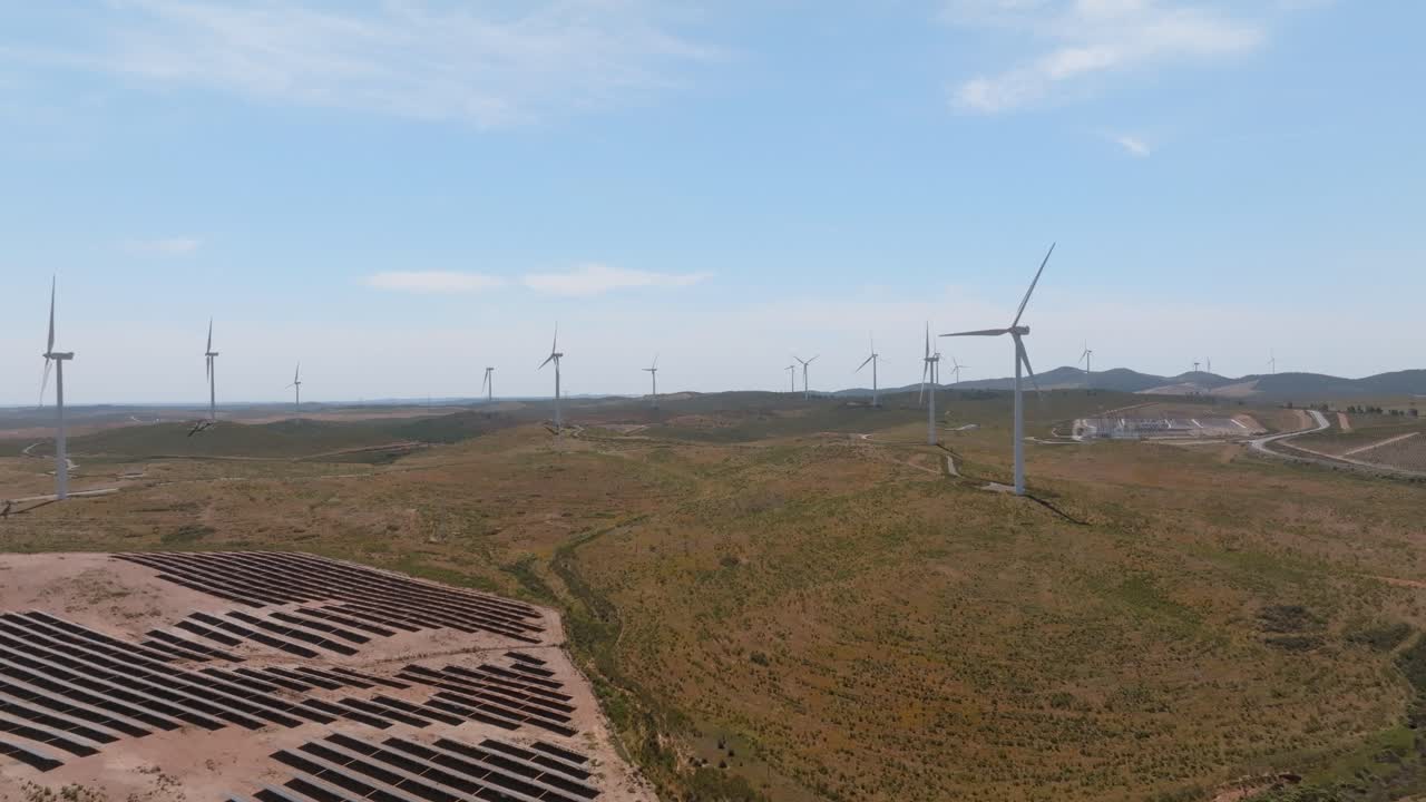 Drone dolly above desert landscape, scattered solar farm field and wind turbines
