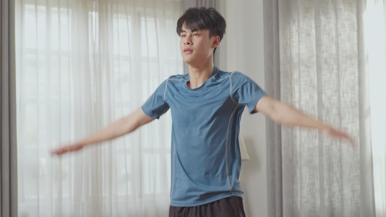 스포츠 옷을 입은 운동 체력의 아시아인 남자가 넓고 밝은 아파트에서 집에서 점핑 잭 운동을 하고 있습니다.
