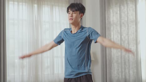 athletic fit asian man in sports clothes is doing jumping jack exercises at home in his spacious and bright apartment
