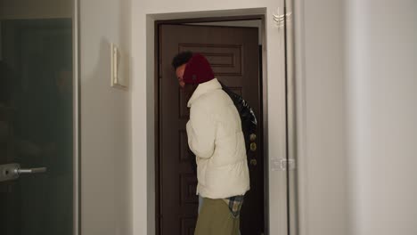 Happy-young-man-with-Black-skin-color-brunette-in-a-black-jacket-comes-home-with-his-young-adult-girlfriend-in-a-plaid-shirt-and-white-jacket-after-a-walk-in-a-modern-apartment