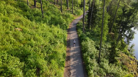 Primer-Plano-De-Un-Dron-Que-Muestra-A-Un-Hombre-Corriendo-Por-Un-Sendero-En-Un-Bosque-Junto-A-Un-Río