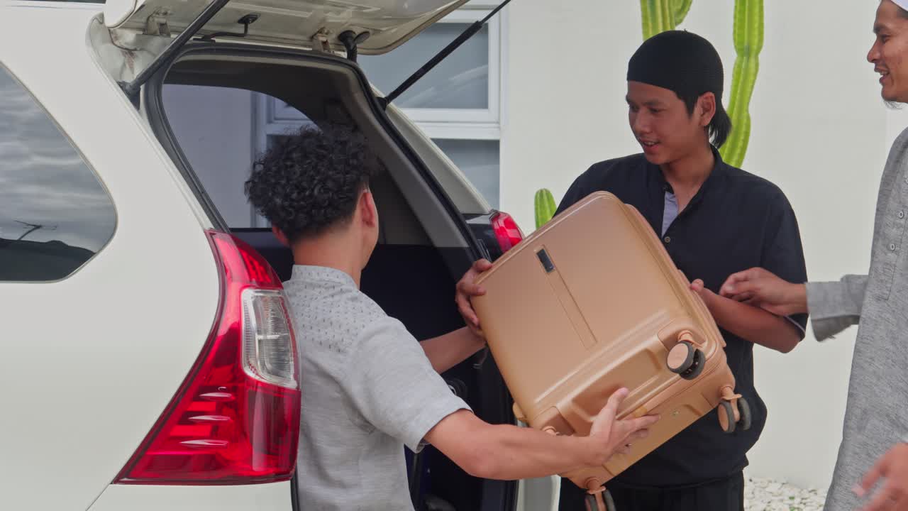 Three young Muslim men loading suitcases into car trunk for Mudik holiday travel