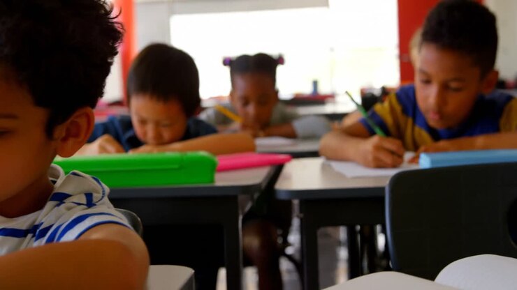 Niños escolares multiétnicos estudiando en sus pupitres en el aula de la escuela 4k
