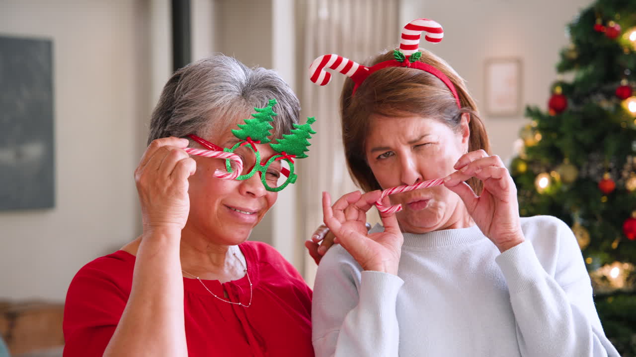 At Christmas, Senior women wearing festive accessories, playfully holding candy canes at home