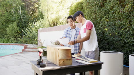 building wooden project, asian father and son reviewing plans and using tools outdoors