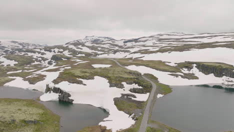 road passing by river and snowy landscape at summer in aurland, norway