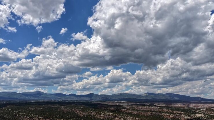 Timelapse 4K UHD con drone: un flusso infinito di drammatiche nuvole cumuliformi si muove su un vasto paesaggio desertico del sud-ovest. Il tempo dinamico proietta ombre in movimento attraverso aspre mesas e montagne distanti.
