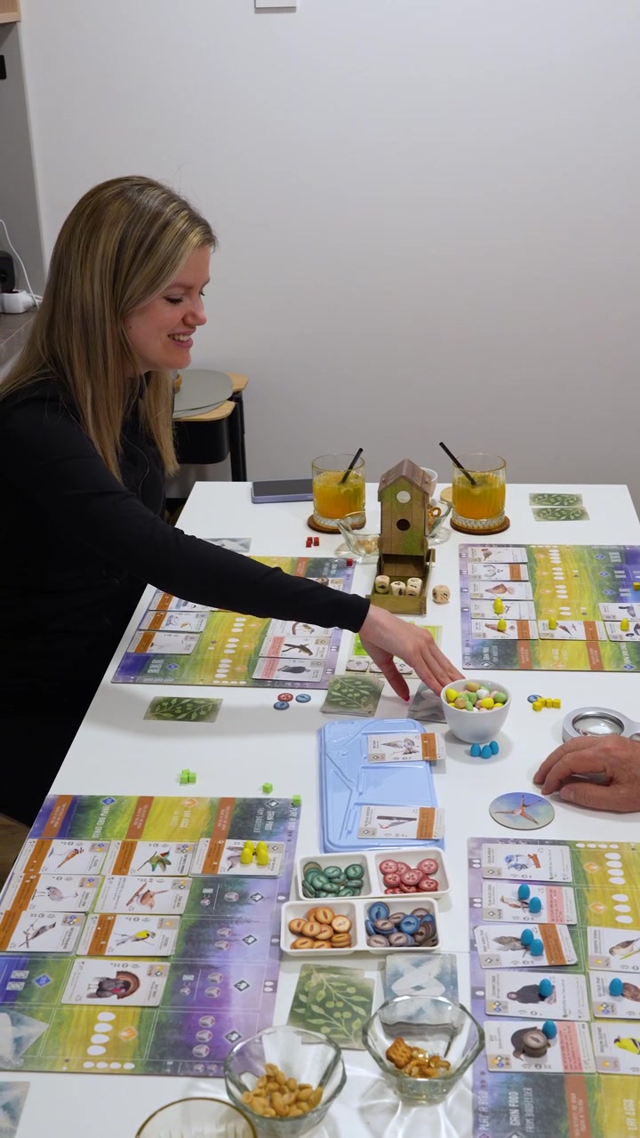Famiglia che si gode una partita a Wingspan insieme a casa durante una serata rilassante, evidenziando l'interazione sociale, il gioco da tavolo e il tempo di qualità trascorso in casa, verticale.