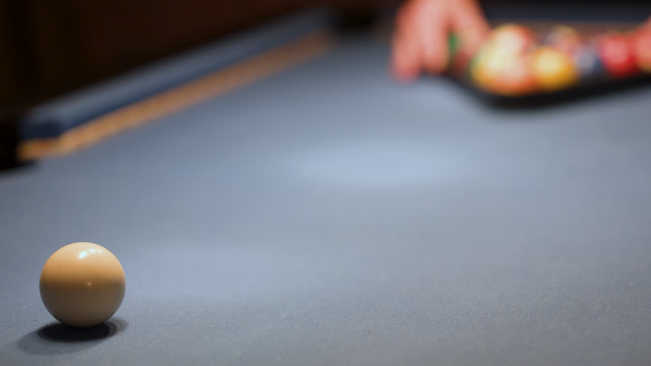 Person arranges colorful pool balls on billiard table in low light, camera remains stationary