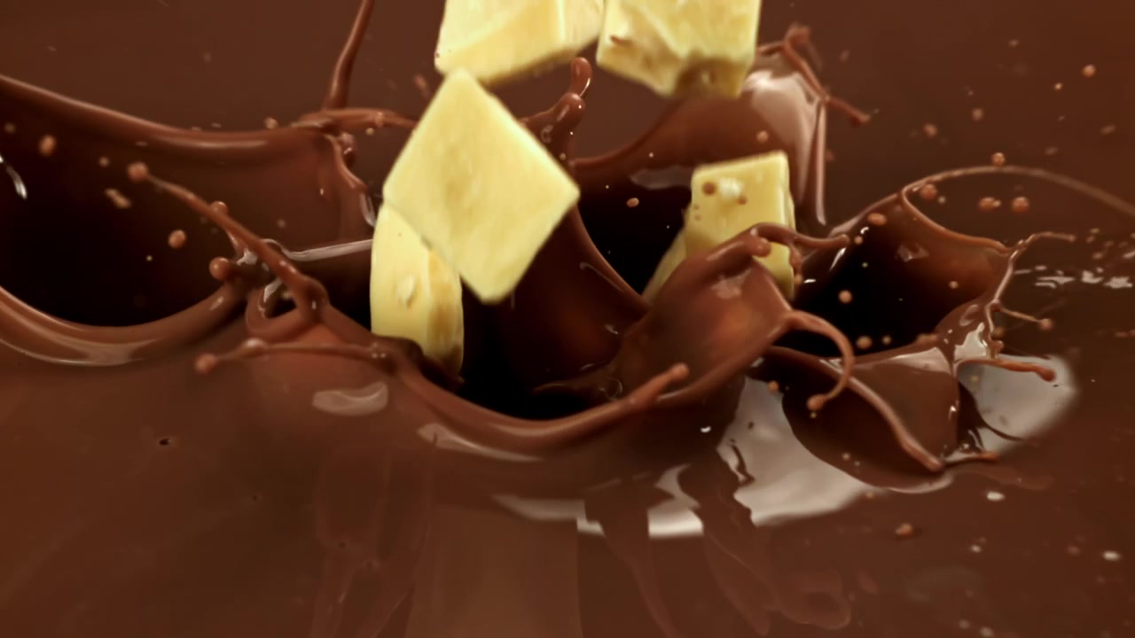 Pezzi di burro di cacao che schizzano nel cioccolato fuso al rallentatore