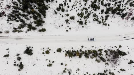 aerial view of a white car driving on snowy road in winter