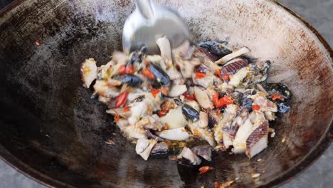 close up shot stirring giant sea snail with sauteed ingredients on wok