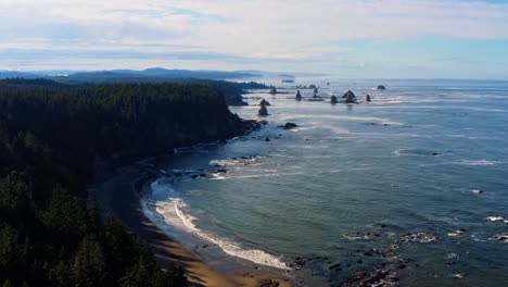 Stunning-aerial-drone-rising-shot-of-the-gorgeous-Third-Beach-in-Forks,-Washington-with-large-rock-formations,-surrounded-by-a-pine-tree-forest-on-cliffs,-and-golden-sand-on-a-warm-summer-morning