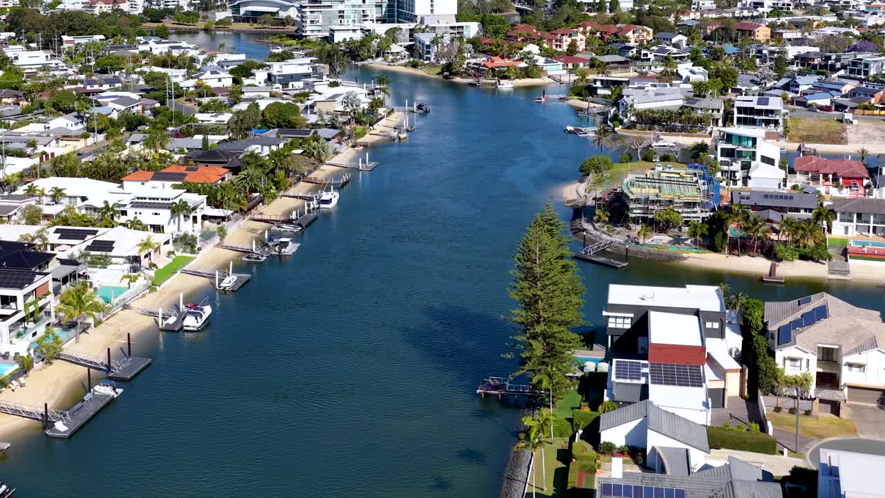 Drone glides above canal, modern waterfront houses, clear daylight, smooth forward camera movement, vibrant scenery