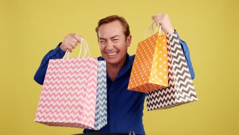 excited man holding up shopping bags on yellow background