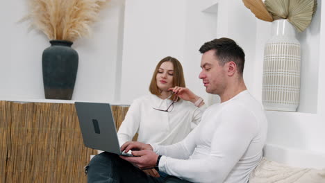 positive caucasian couple sitting on the sofa and looking at laptop. people working on internet remote.