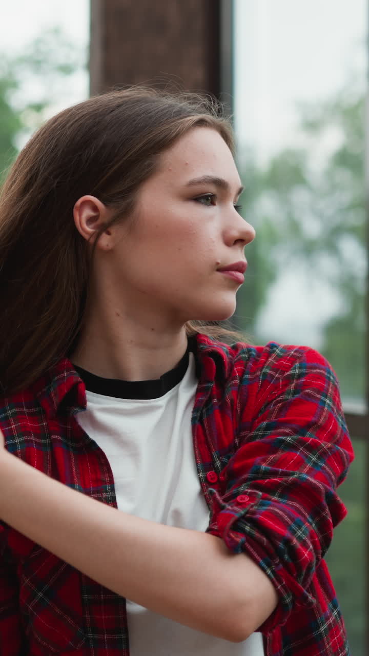 los dedos de la dama meten el cabello suelto detrás de la oreja. los gestos delicados de la mujer transmiten una sensación de introspección y contemplación tranquila cerca de las ventanas panorámicas