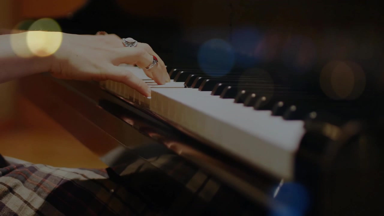 Eine Musikerin legt ihre Hand auf die Klaviertasten, bevor sie Akkorde in einem Musikstudio mit Bokeh-Lichtern spielt.