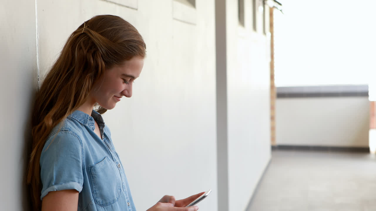 Scolara felice che usa il telefono cellulare nel corridoio