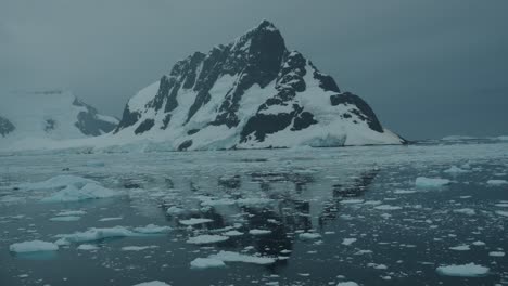 Slowly-cruising-through-Antarctic-waters-with-reflection-of-snow-capped-mountains-in-the-background-at-sunrise