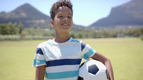 biracial boy holds a soccer ball in school, smiling in a sunny park