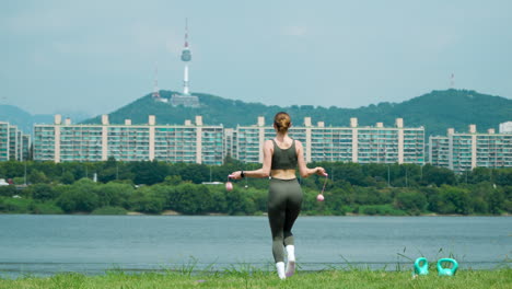 fittness woman trains with cordless jump rope jumping on one leg at han river park with famous n seoul namsan tower in background