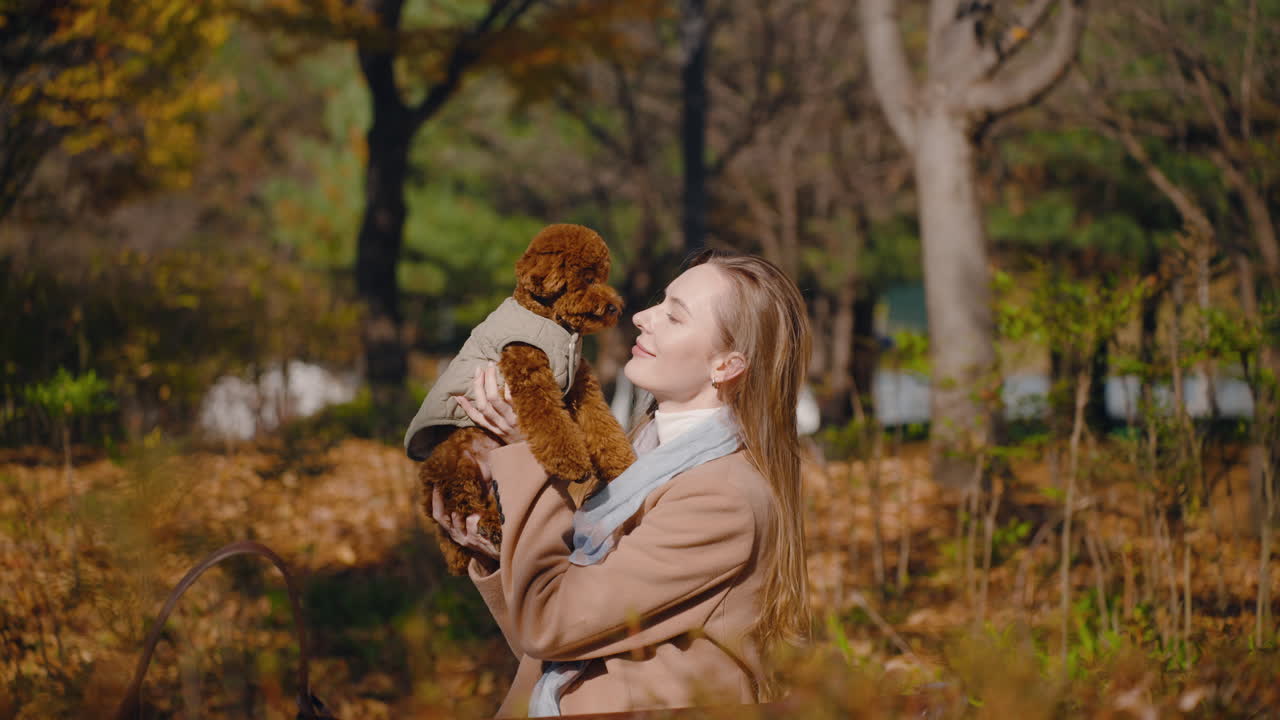 Woman holding her adorable brown poodle in an autumn park