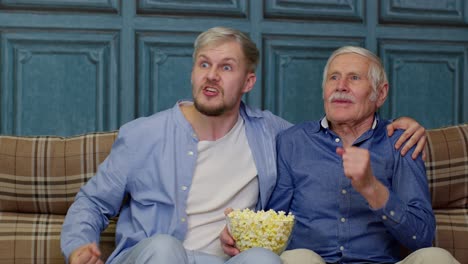 two men high five while watching tv and eating popcorn