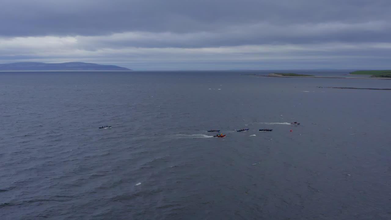Sideview aerial of currach boat canoes paddling in open ocean with support vessel near by