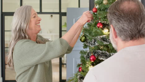 Decorating Christmas tree with ornaments, mature couple embracing holiday spirit