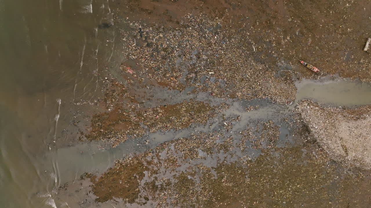 Toma aérea cenital de un arroyo depositando basura en el océano.